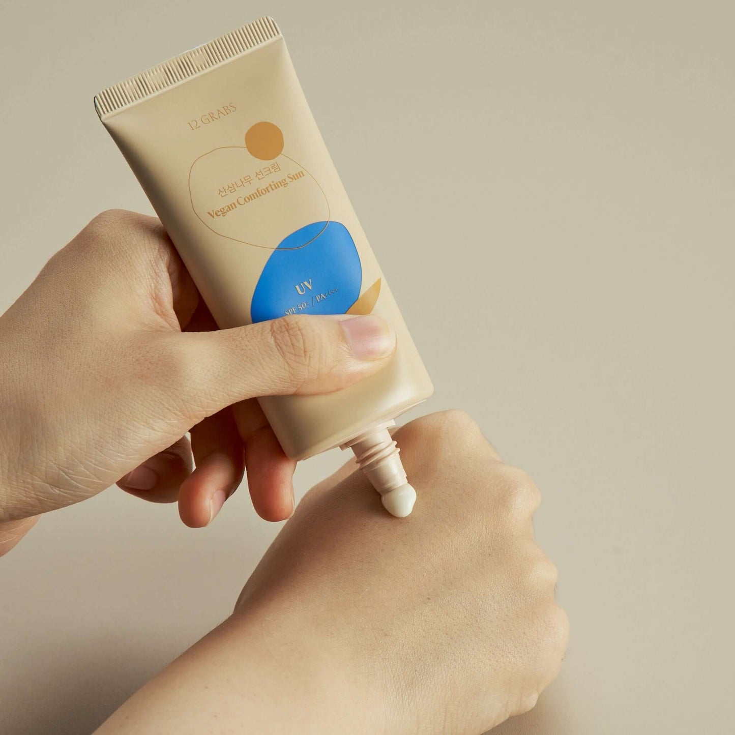 12GRABS Vegan Comforting Sun SPF50+ PA++++ tube being applied to hand, showcasing vegan mineral sunscreen SPF50.
